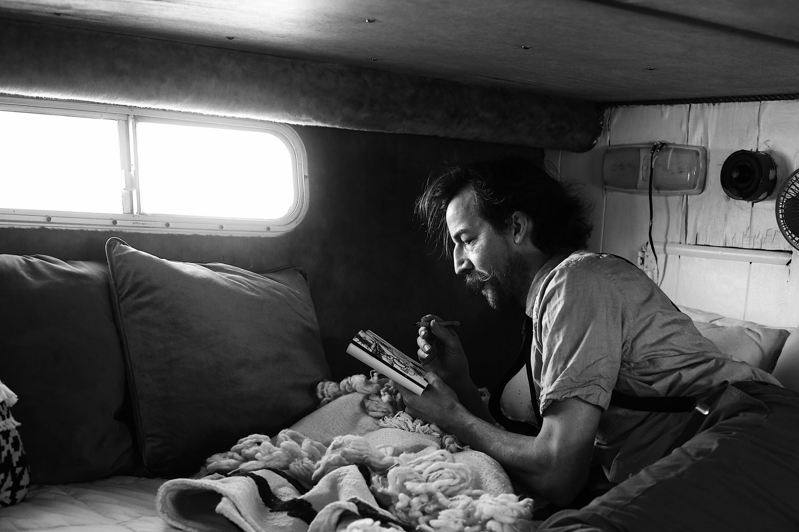 black and white photograph of an artist in a mustache and button down sketching while in the cabin of a boat -bisoux de lune meagan reily