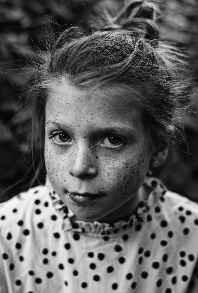 portait of a young freckle faced girl in black and white in a polka dot shirt with high contrast and a very serious face - bisoux de lune meagan reily