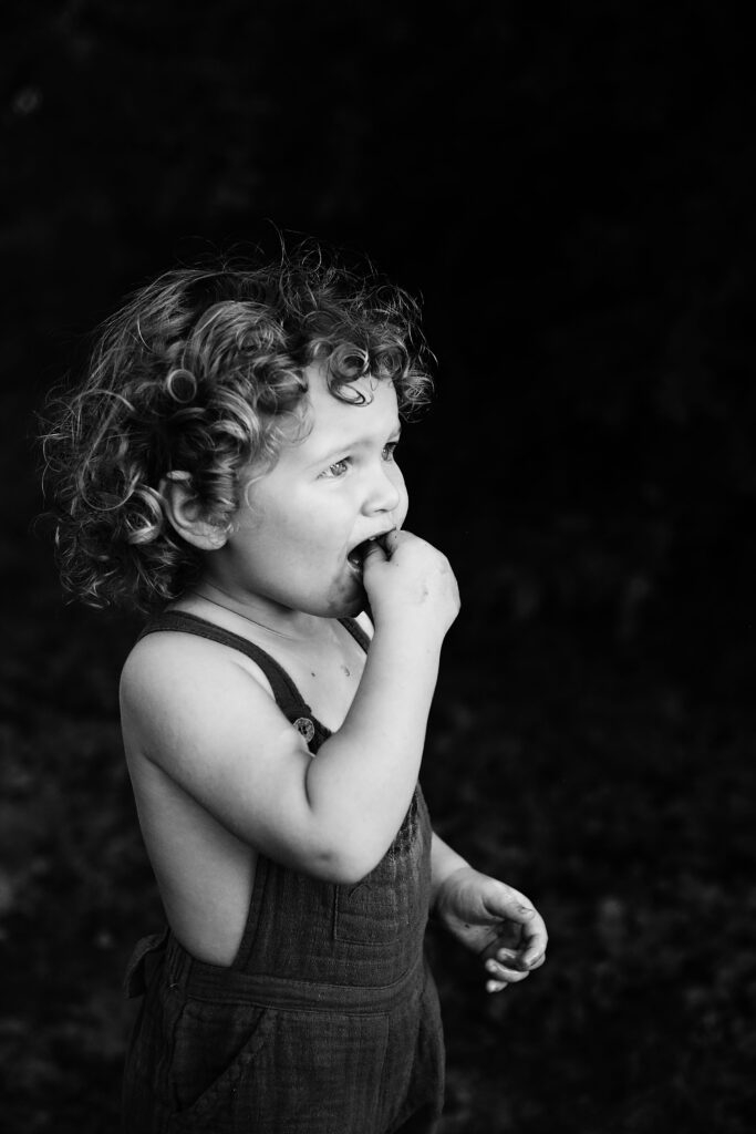 child wearing overalls biting apple - - Bisoux De Lune