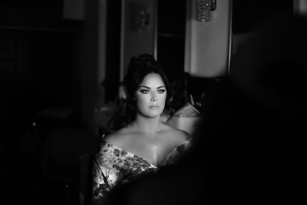 black and white portrait of a black haired bride in full make up getting ready with her make up artist in a floral robe -bisoux de lune meagan reily