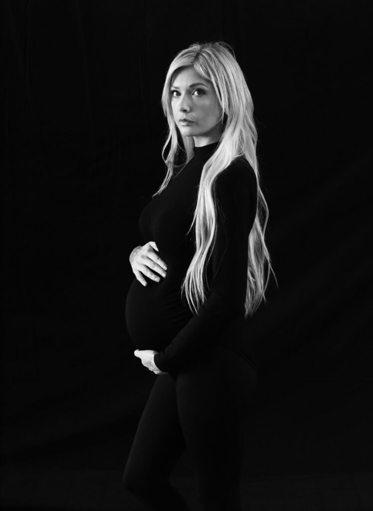 black and white maternity photo of a blonde woman with long hair and her hands on her belly and a model face -bisoux de lune meagan reily