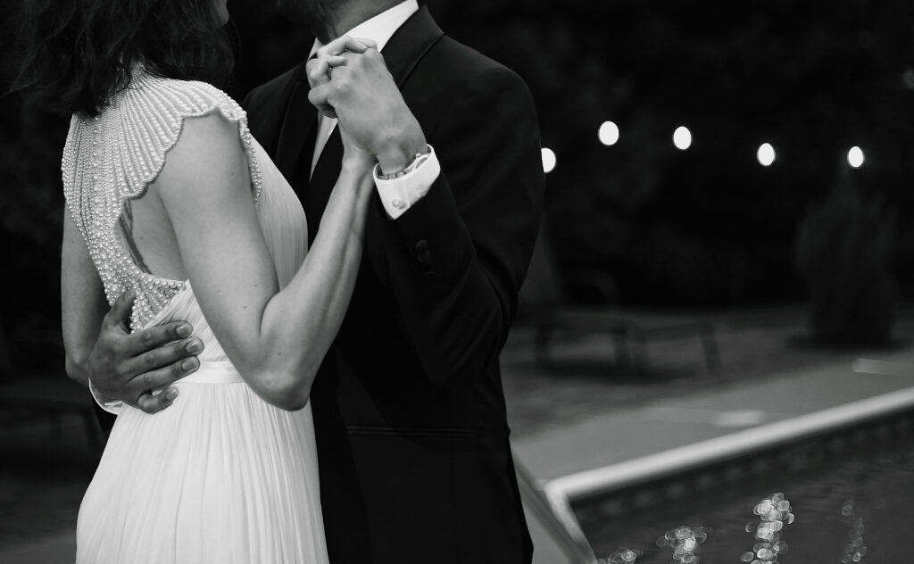 up close black and white photograph of bride and groom dancing next to a pool while they hold hands bride wears a beaded vintage gown -bisoux de lune meagan reily