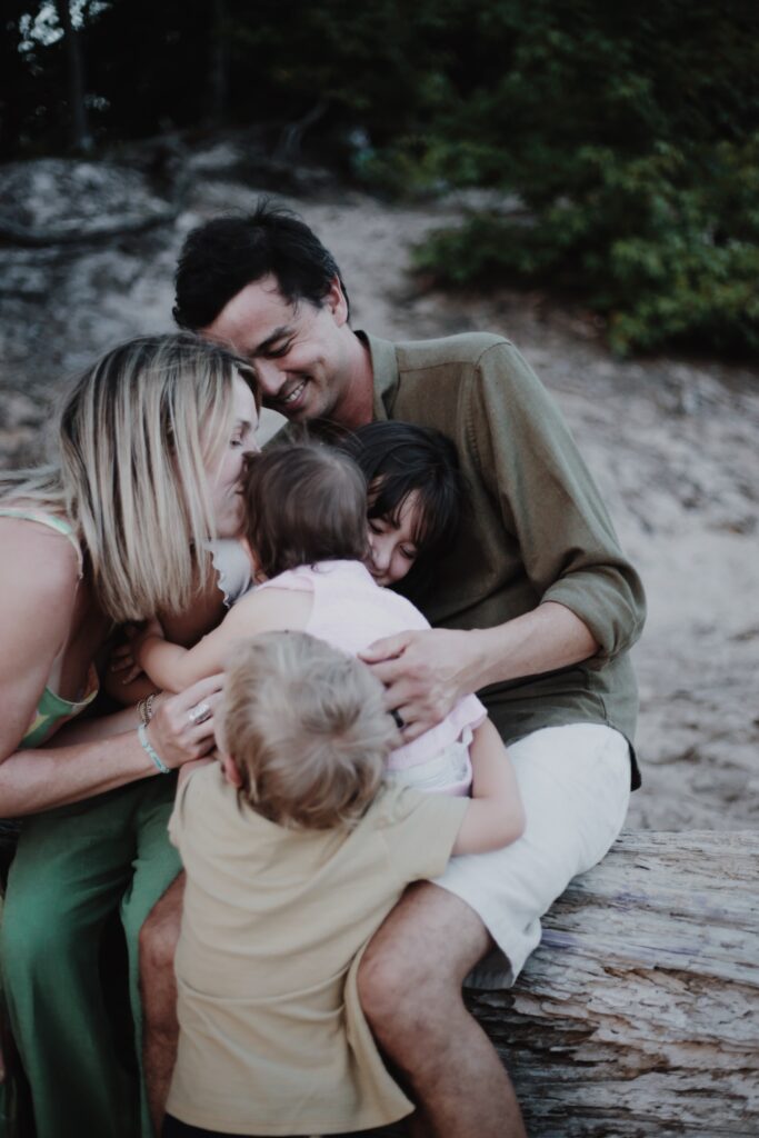 color photograph in neutral tones depicting a blonde mother and dark haired father hugging their three young children and smiling -bisoux de lune meagan reily