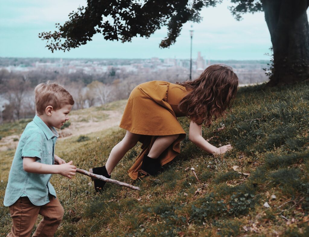 warm colored photograph in richmond virginia of two children a boy and a girl climbing a flowered hill with a big tree and cityscape in the background -bisoux de lune meagan reily