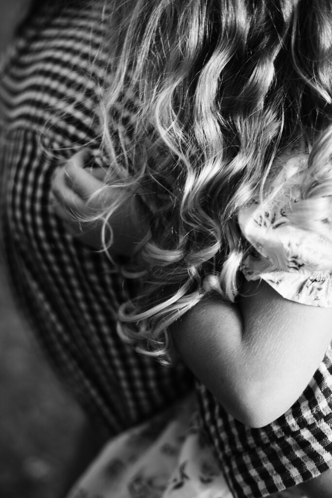 up close black and white portait of a curly blonde haired little girl being held by her mom in a black and white gingham top -bisoux de lune meagan reily