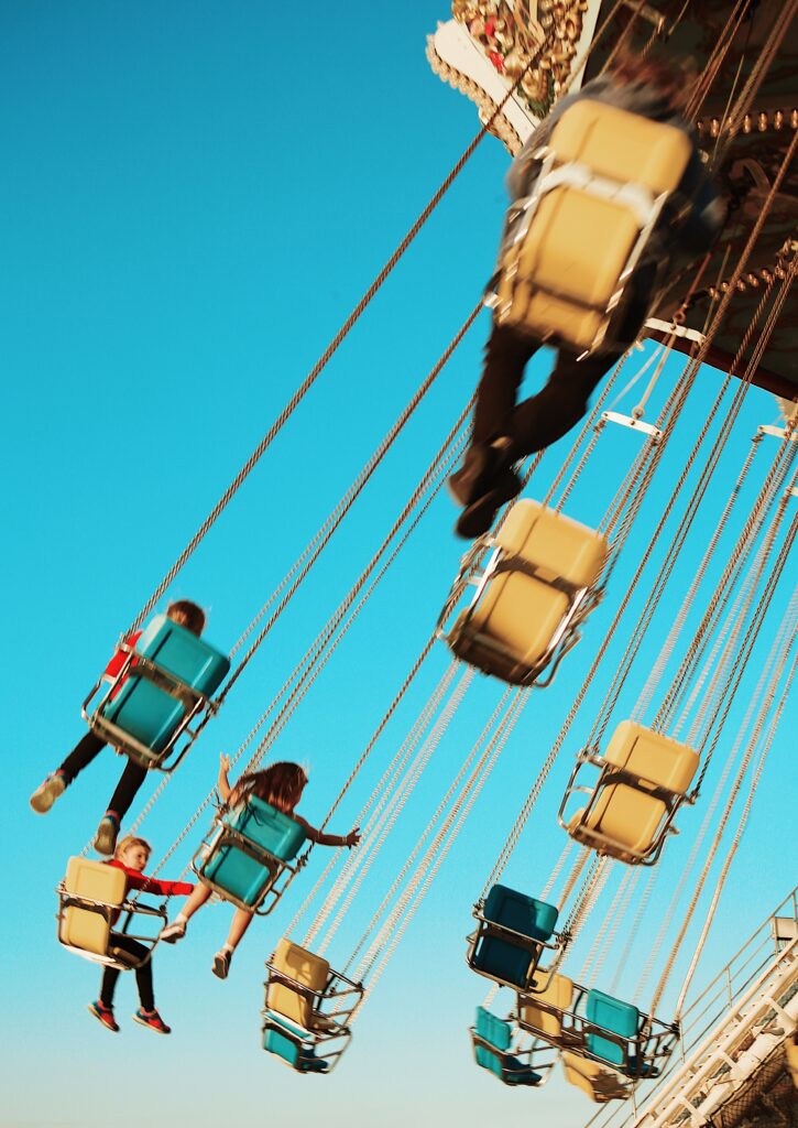 bright retro blue carousel swings with children flying through the air with their hands up -bisoux de lune meagan reily